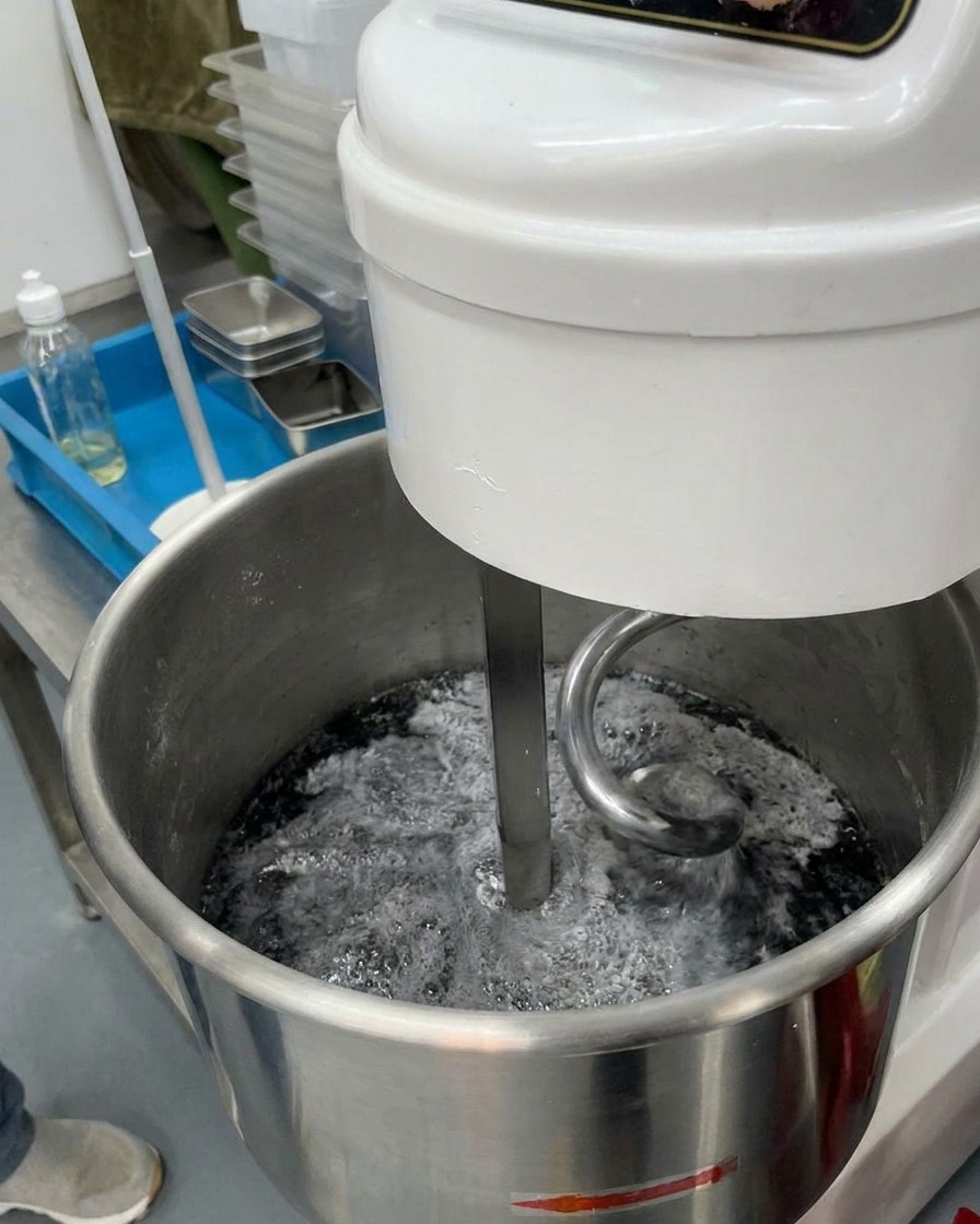 Agua helada vertiéndose en un bol de amasadora que contiene una mezcla de harina gris oscura.