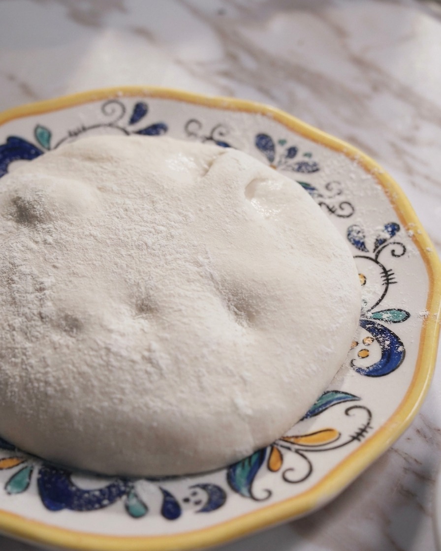 Una bola de masa de pizza napolitana fermentada y suave en un plato cerámico decorativo.