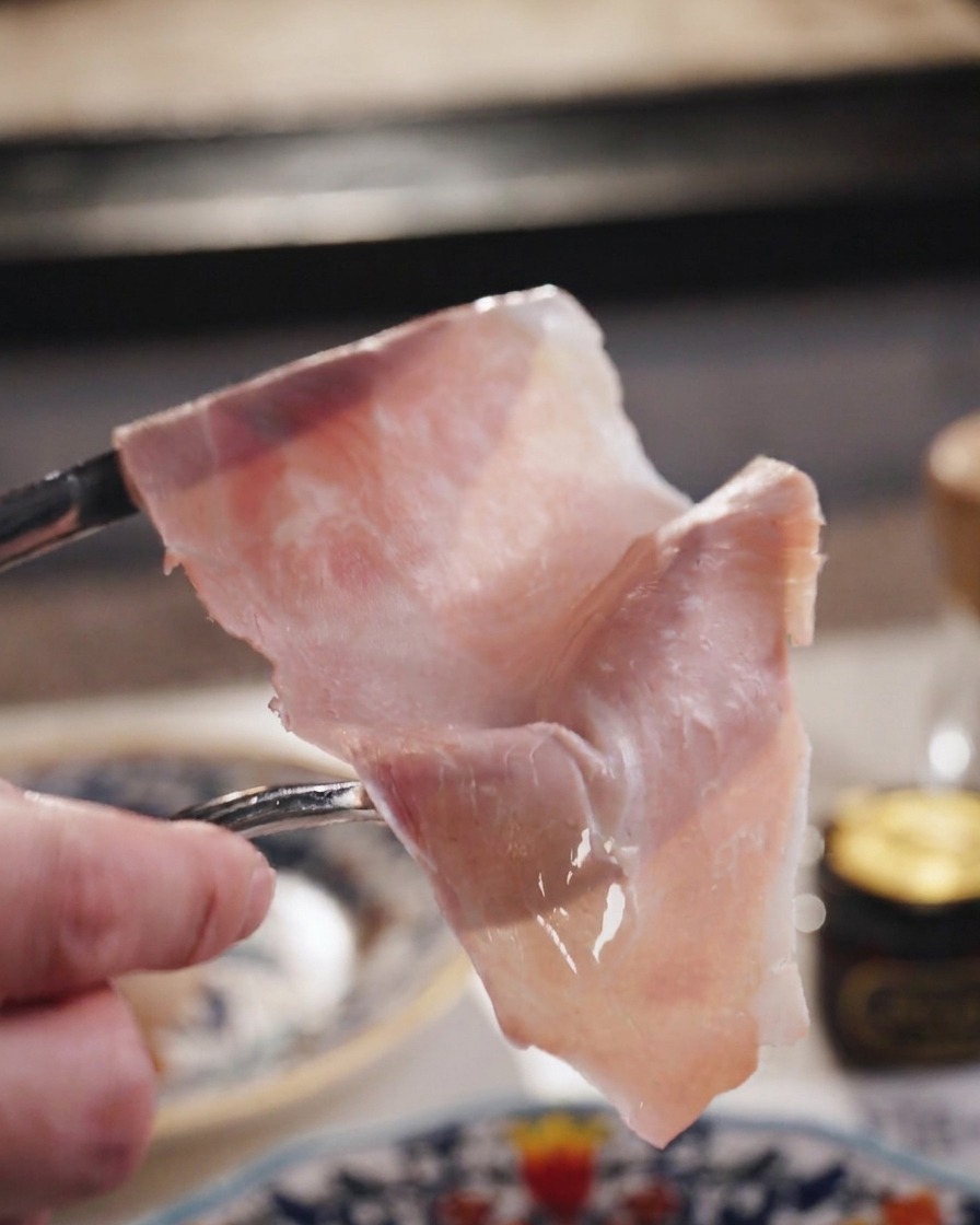 Una loncha fina y traslúcida de jamón sostenida por un tenedor.