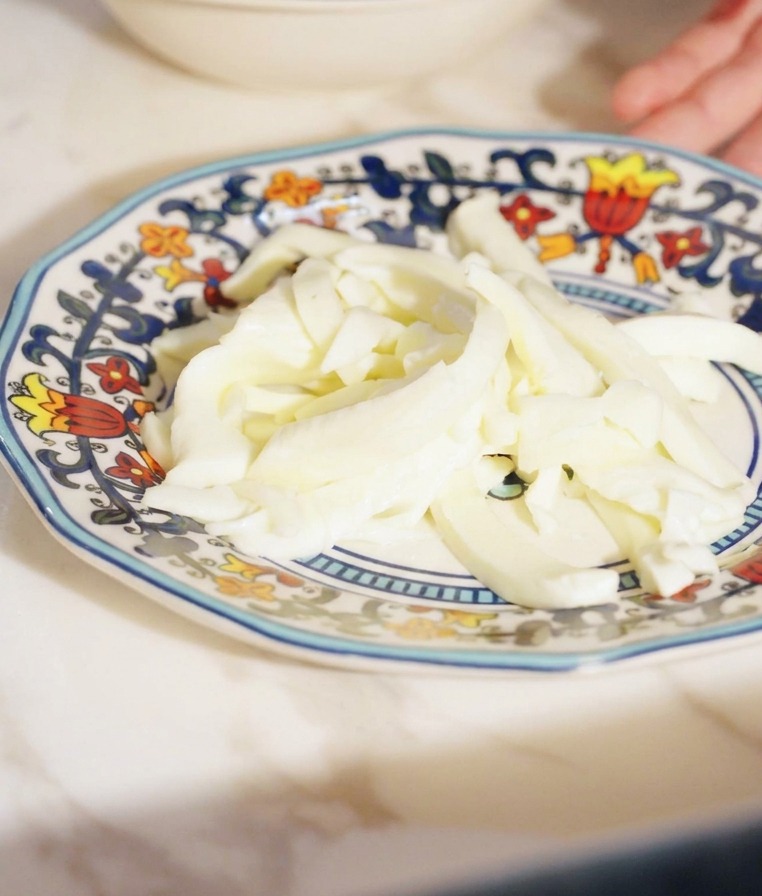 Tiras uniformes de queso fior di latte blanco apiladas en un plato pequeño.