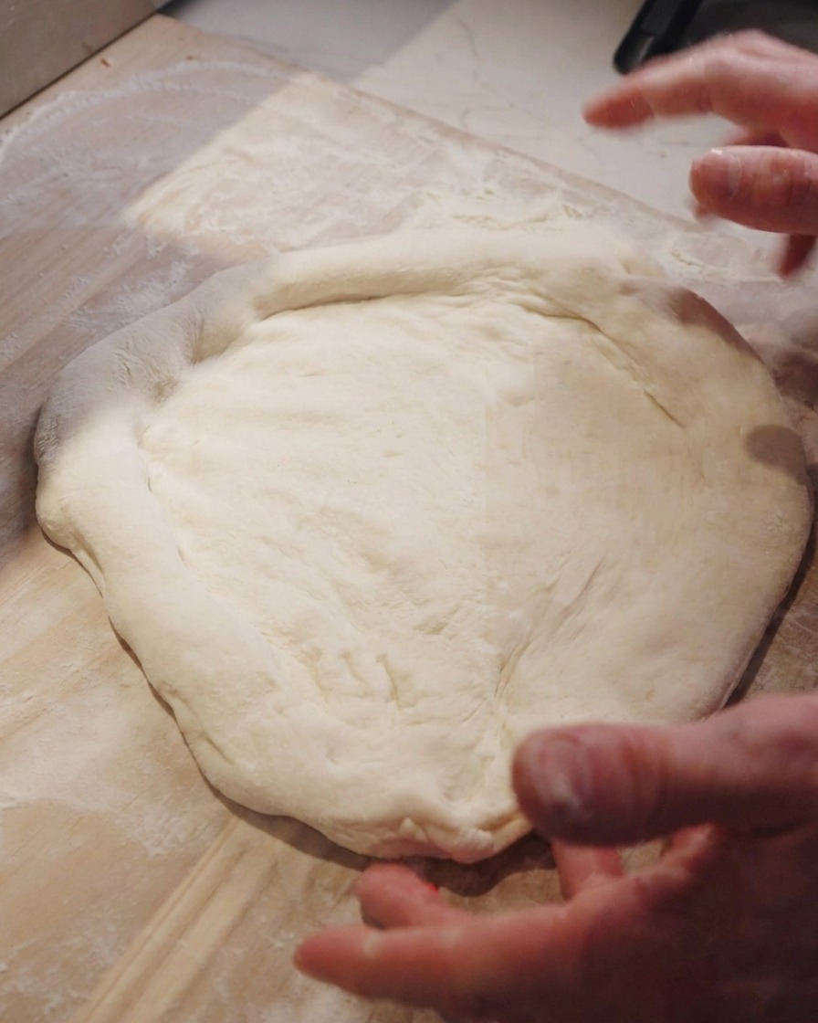 Manos de un chef estirando la masa de pizza sobre un mostrador de madera.