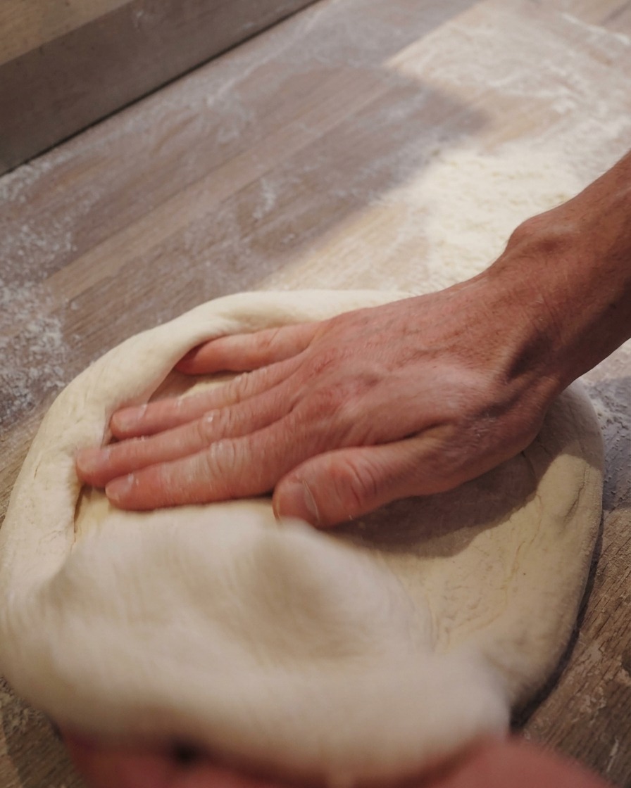 Manos estirando un disco de masa de pizza sobre una superficie con harina.