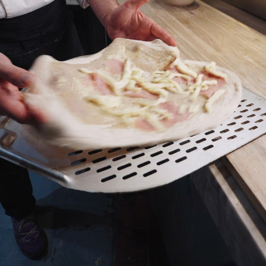 Chef sosteniendo la pizza cruda en una pala metálica con trufa, jamón y queso.