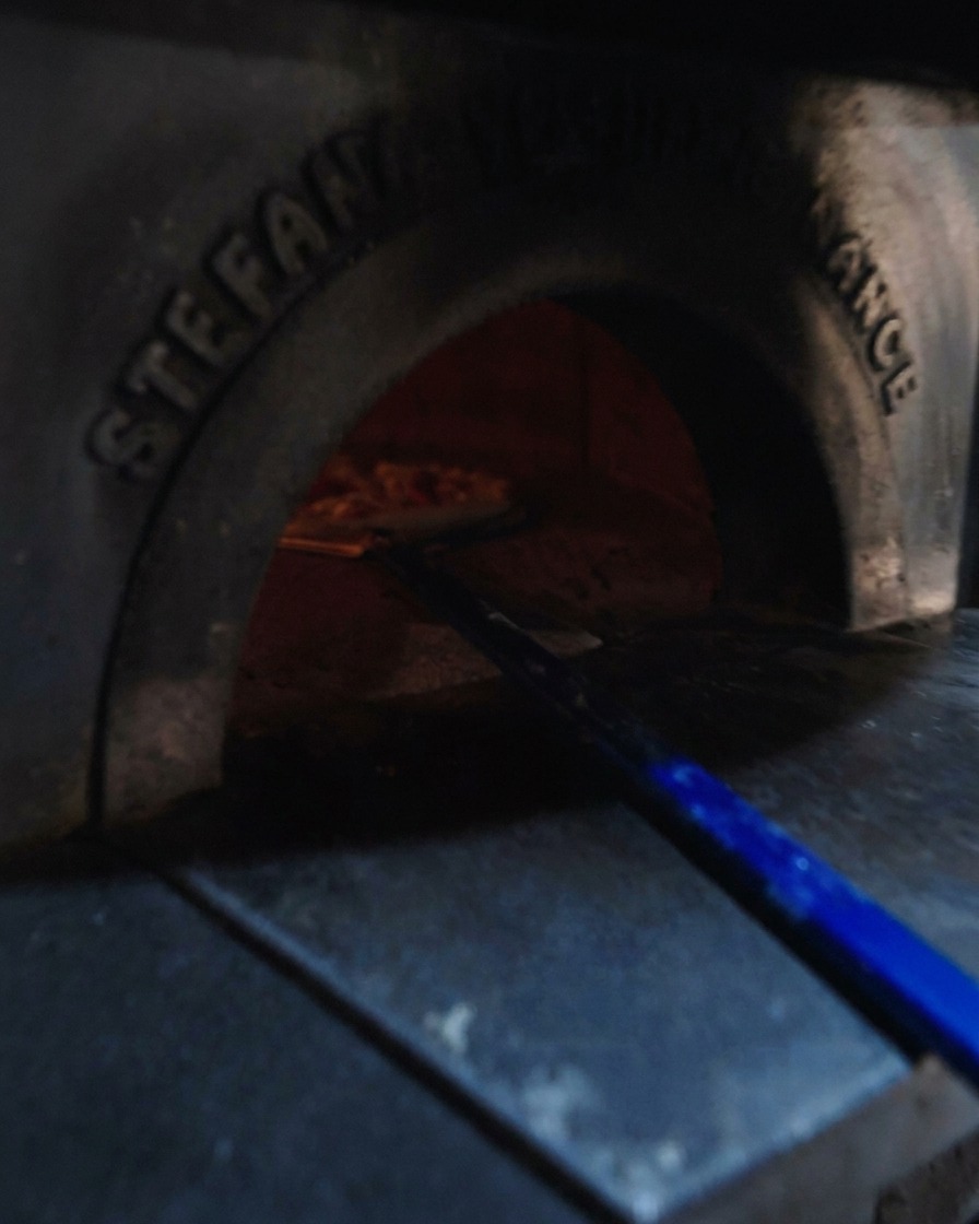 Pala de pizza deslizando la masa en un horno de leña al rojo vivo.