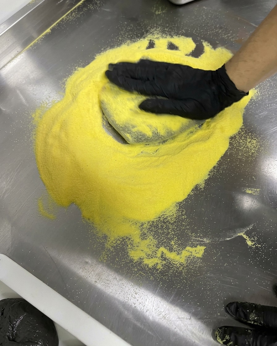 Manos con guantes estirando masa negra en círculo sobre una superficie de acero inoxidable enharinada.