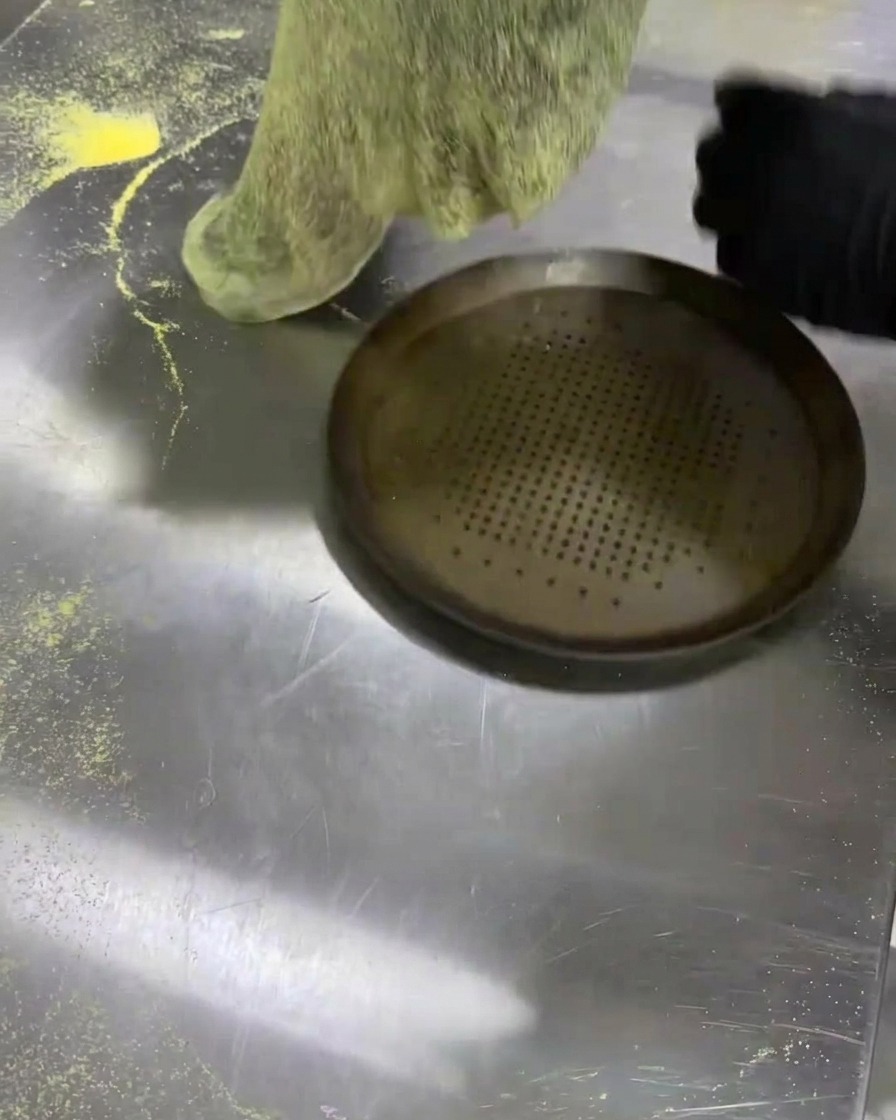 Colocando la masa negra estirada sobre una bandeja para pizza metálica perforada.