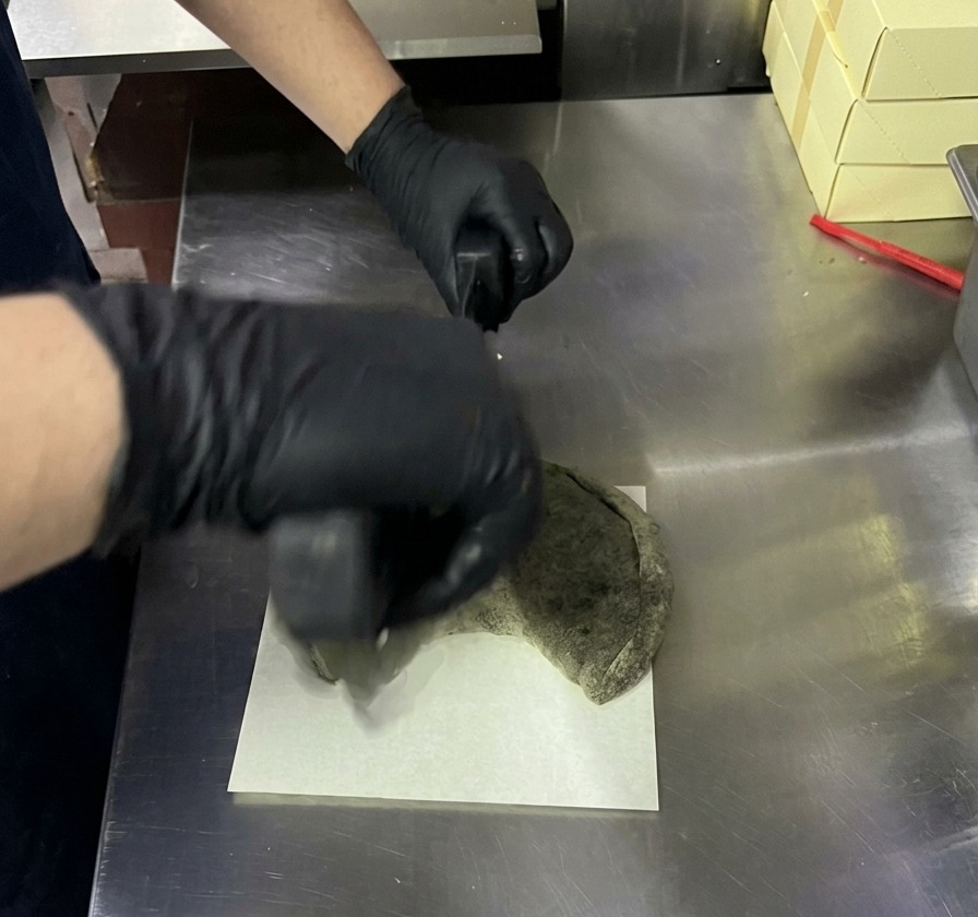 Cortando un calzone negro horneado con un cortador de pizza curvo sobre una tabla blanca.