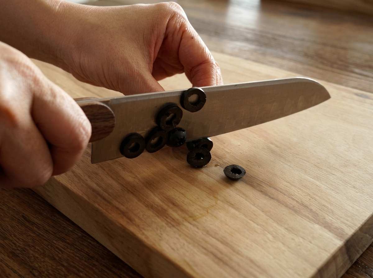Manos cortando aceitunas negras sin hueso en aros sobre una tabla de madera.