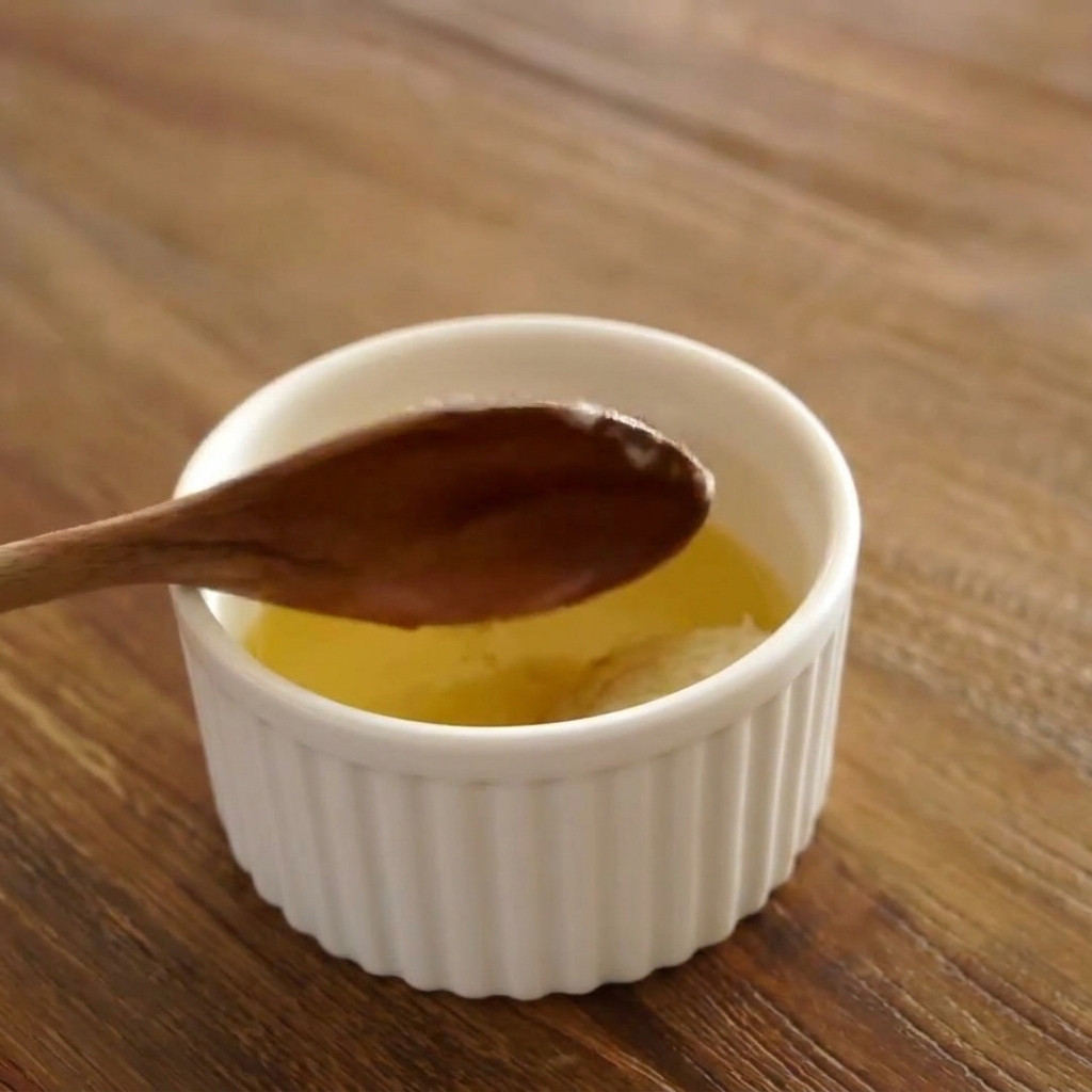 Una cuchara removiendo una mezcla de mantequilla derretida, ajo y miel en un cuenco pequeño.