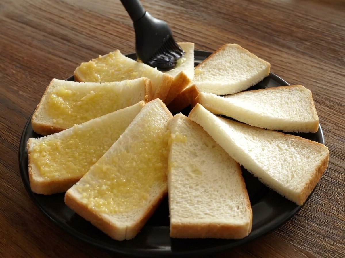 Pincel de silicona aplicando mantequilla de ajo sobre los bordes del pan dispuestos en círculo.