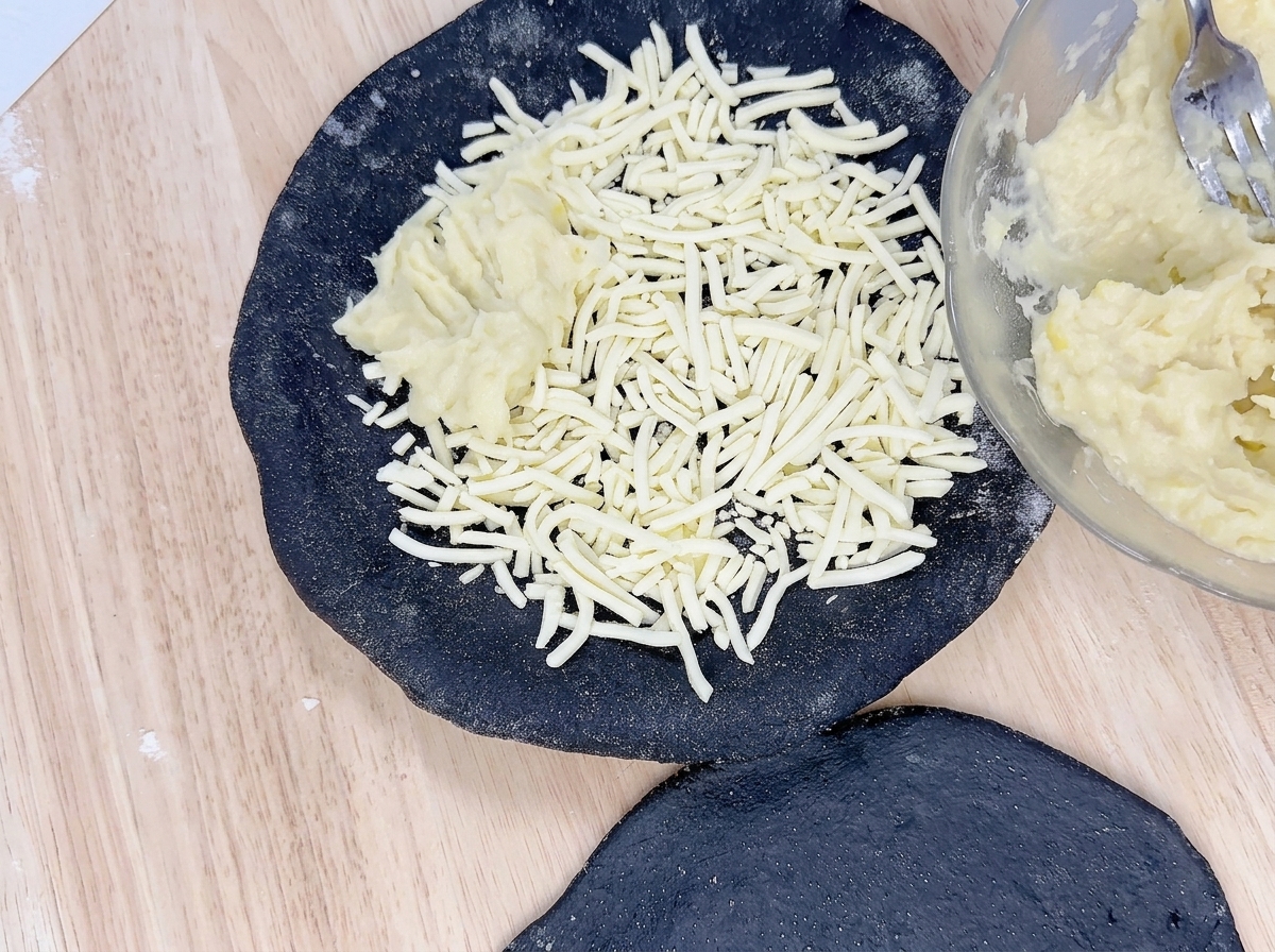 Durián amarillo siendo servido con cuchara sobre el queso en la masa de pizza negra.