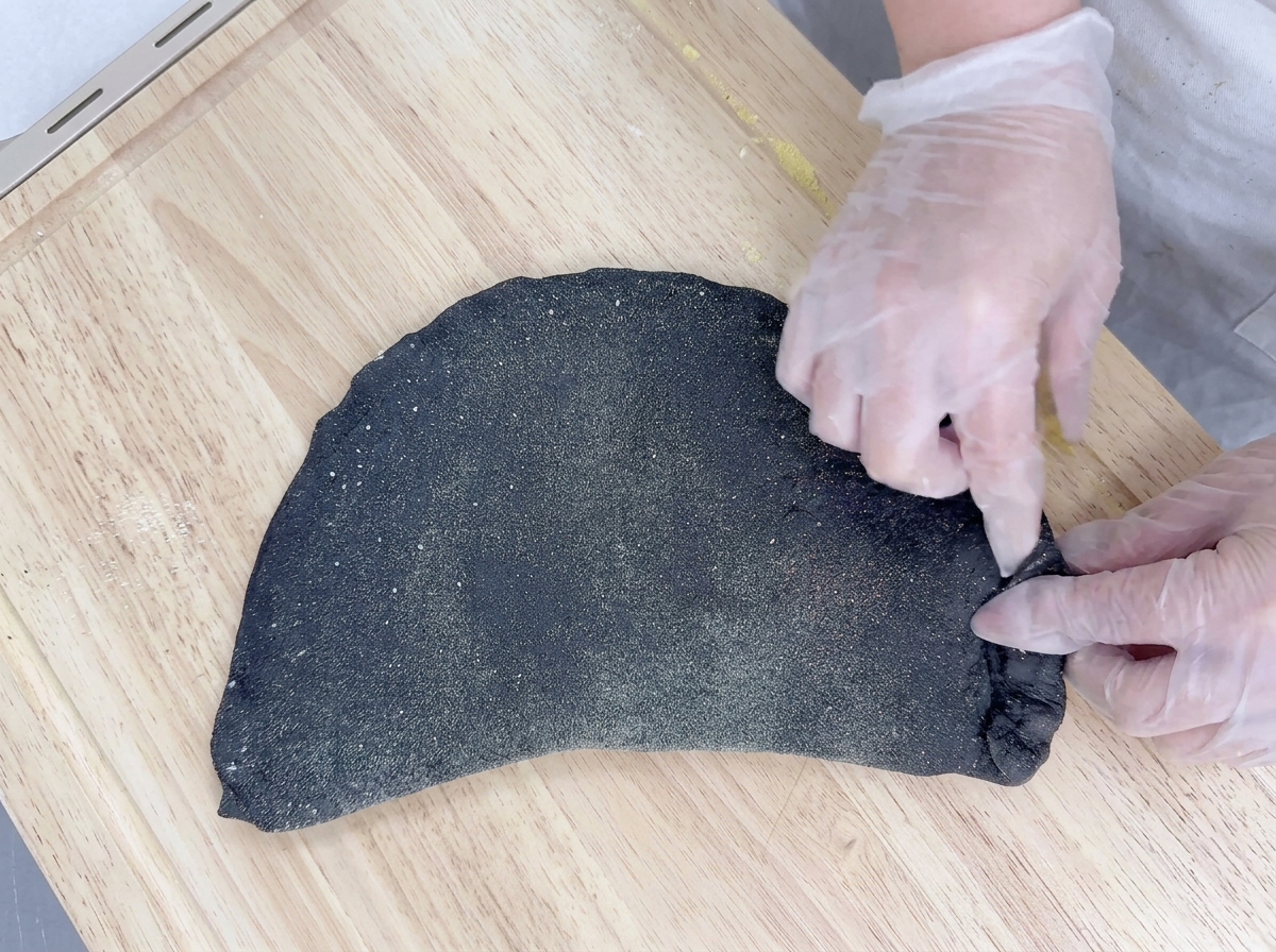 Manos con guantes doblando la masa ovalada por la mitad y sellando los bordes.