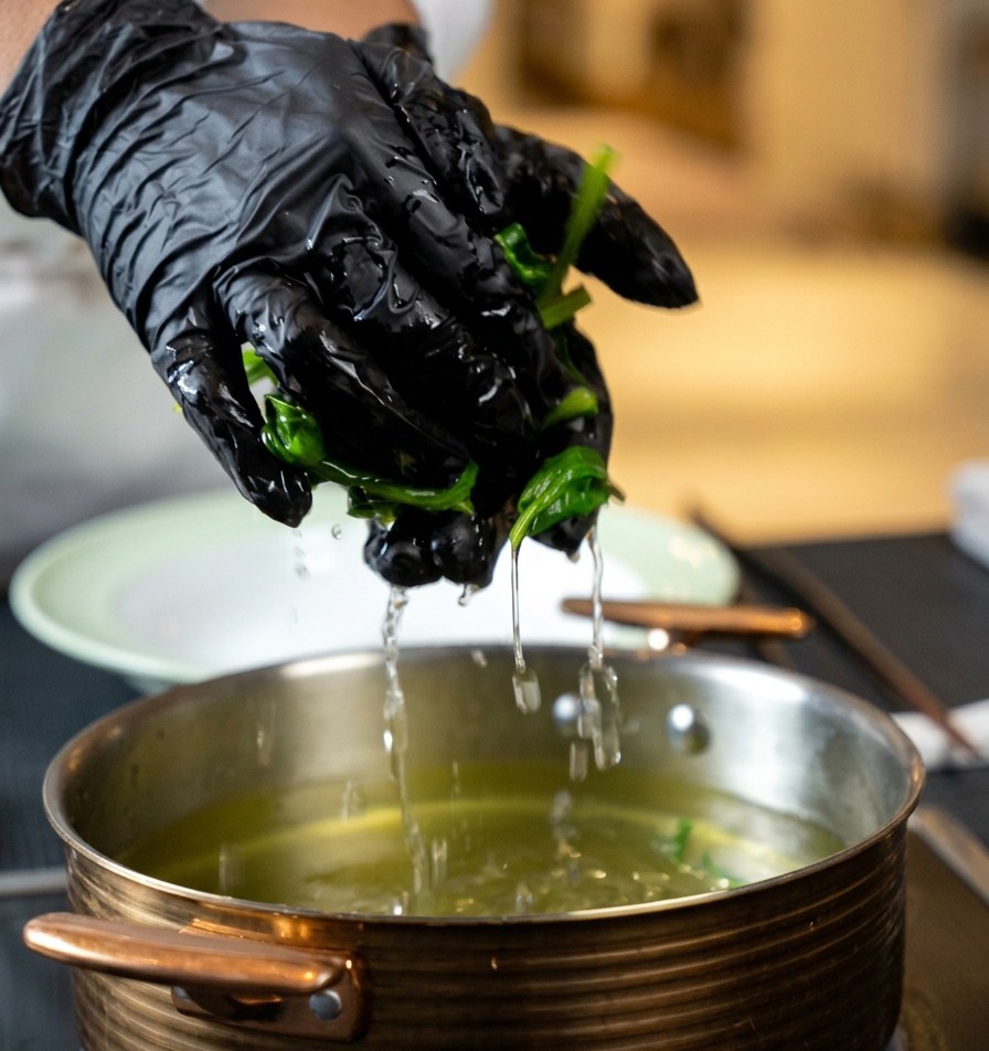 Manos escurriendo con fuerza un puñado de espinacas cocidas sobre una olla.
