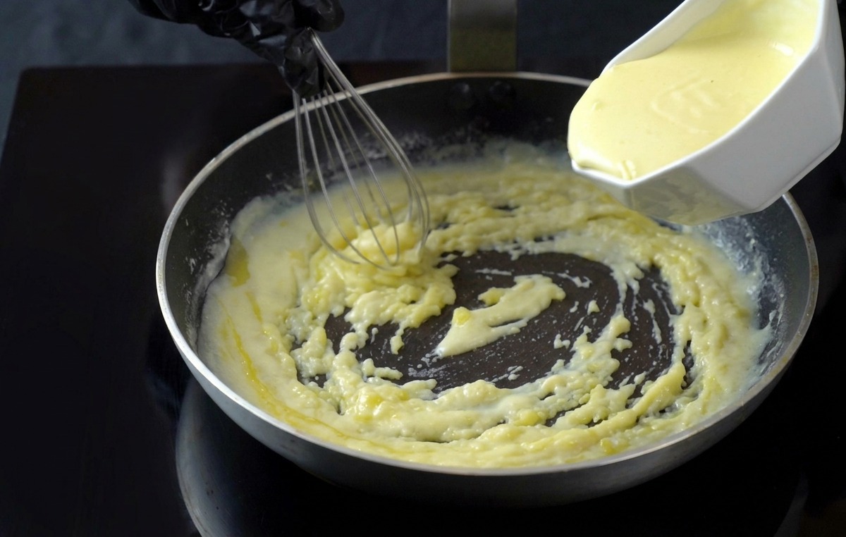 Vertiendo crema de leche en la salsa blanquecina de la sartén.
