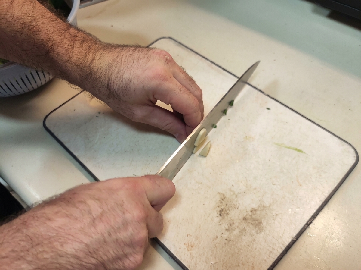 Manos picando finamente dientes de ajo sobre una tabla de cortar blanca.