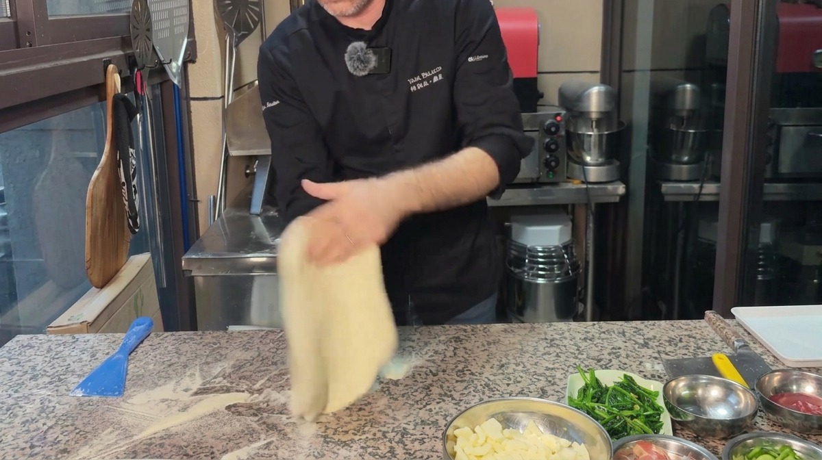 Chef estirando la masa de pizza en forma de círculo sobre una superficie de mármol enharinada.