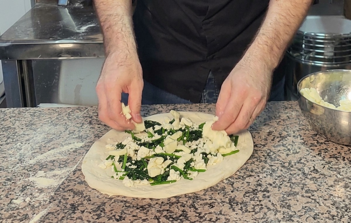 Añadiendo trozos de queso mozzarella sobre las espinacas y el feta en una pizza cruda.