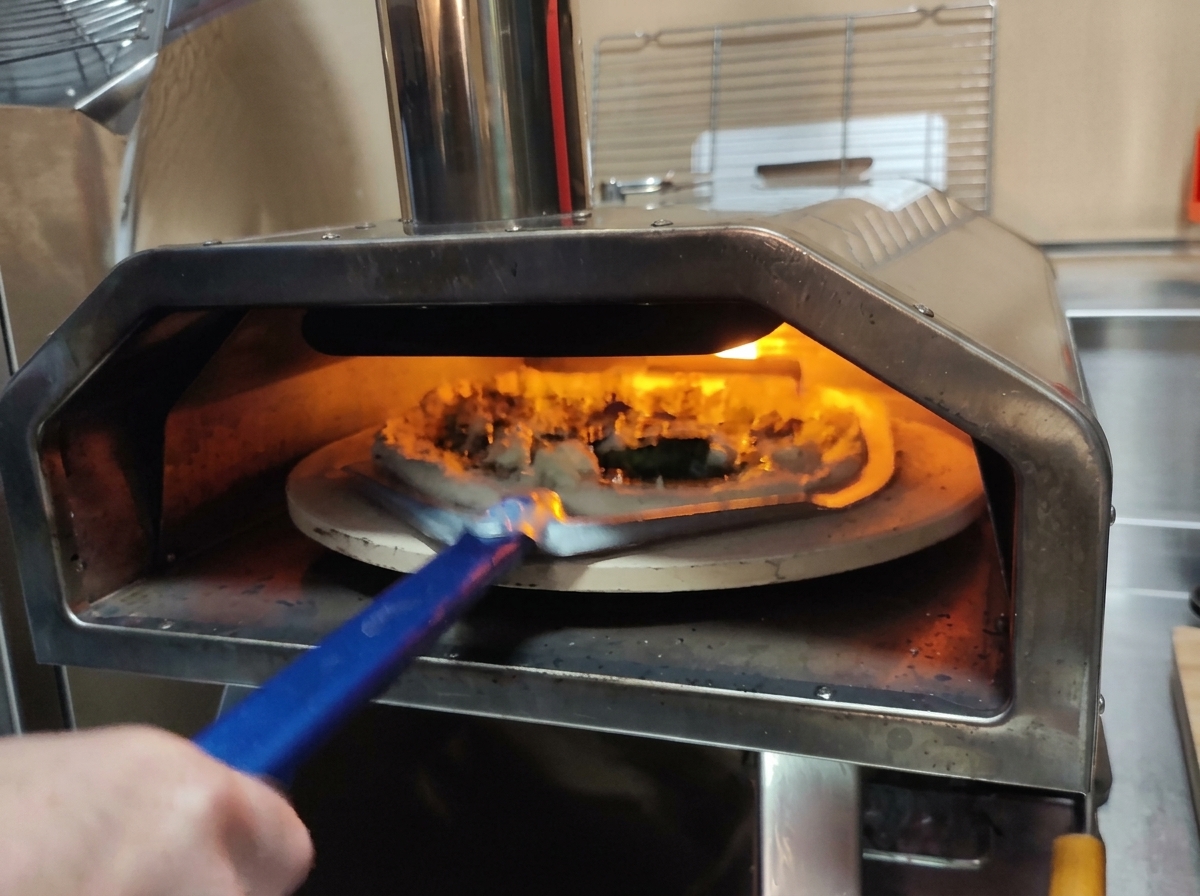 Usando una pala de pizza perforada para introducir la pizza cruda en un horno encendido.