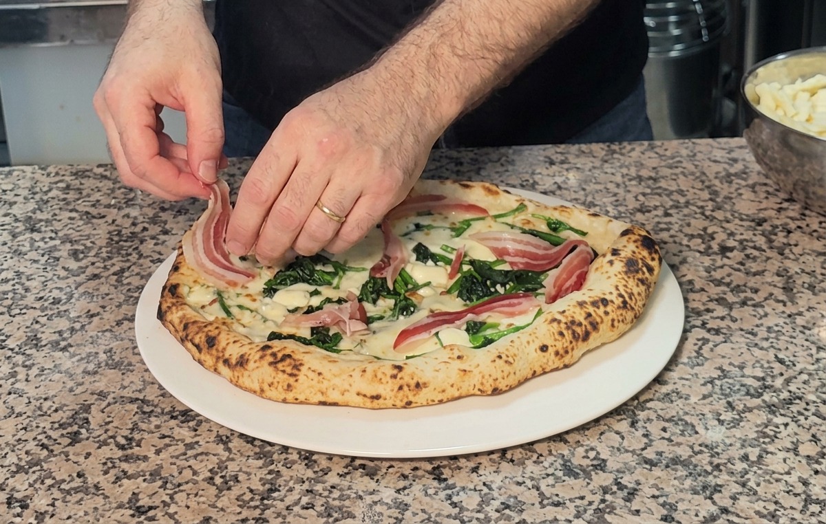 Colocando finas lonchas de panceta sobre una pizza de espinacas y queso recién horneada.