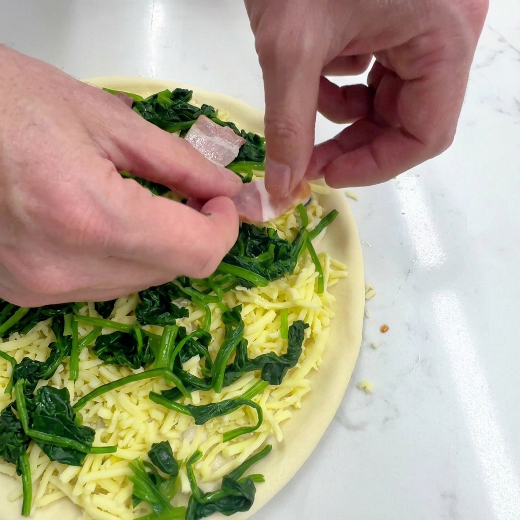Manos colocando cuidadosamente trozos de beicon crudo sobre la pizza con espinacas y queso.