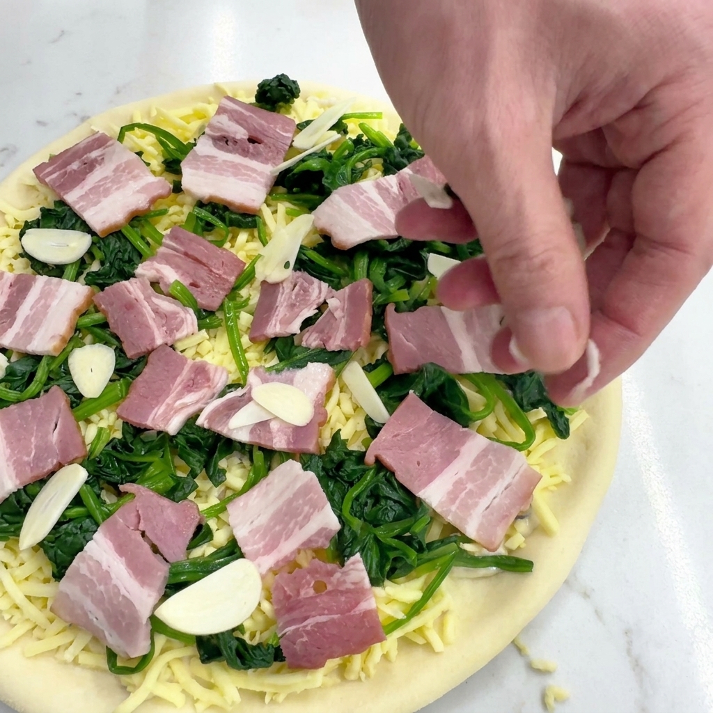 Una mano esparciendo láminas de ajo crudo sobre la pizza con espinacas, beicon y mozzarella.