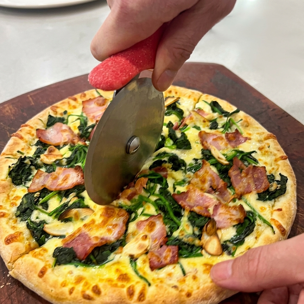 Manos usando un cortapizzas circular para cortar la pizza caliente sobre una tabla de madera oscura.