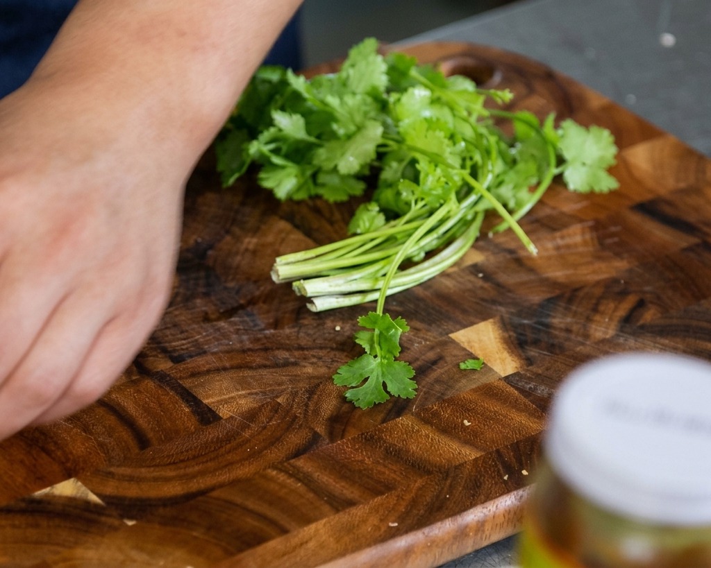 Hojas y tallos de cilantro fresco reposando en una tabla de madera, listos para ser picados a mano.