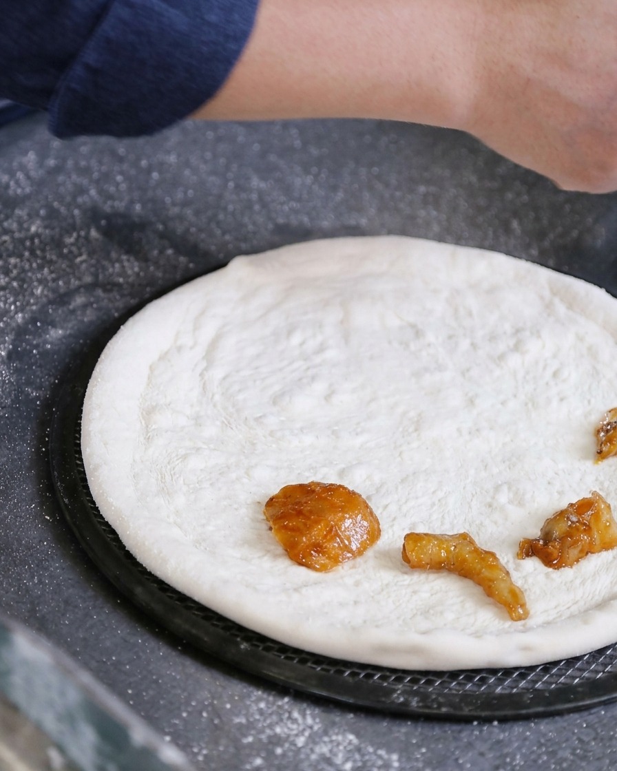 Una mano colocando trozos de marisco marinado directamente sobre una masa de pizza blanca estirada.