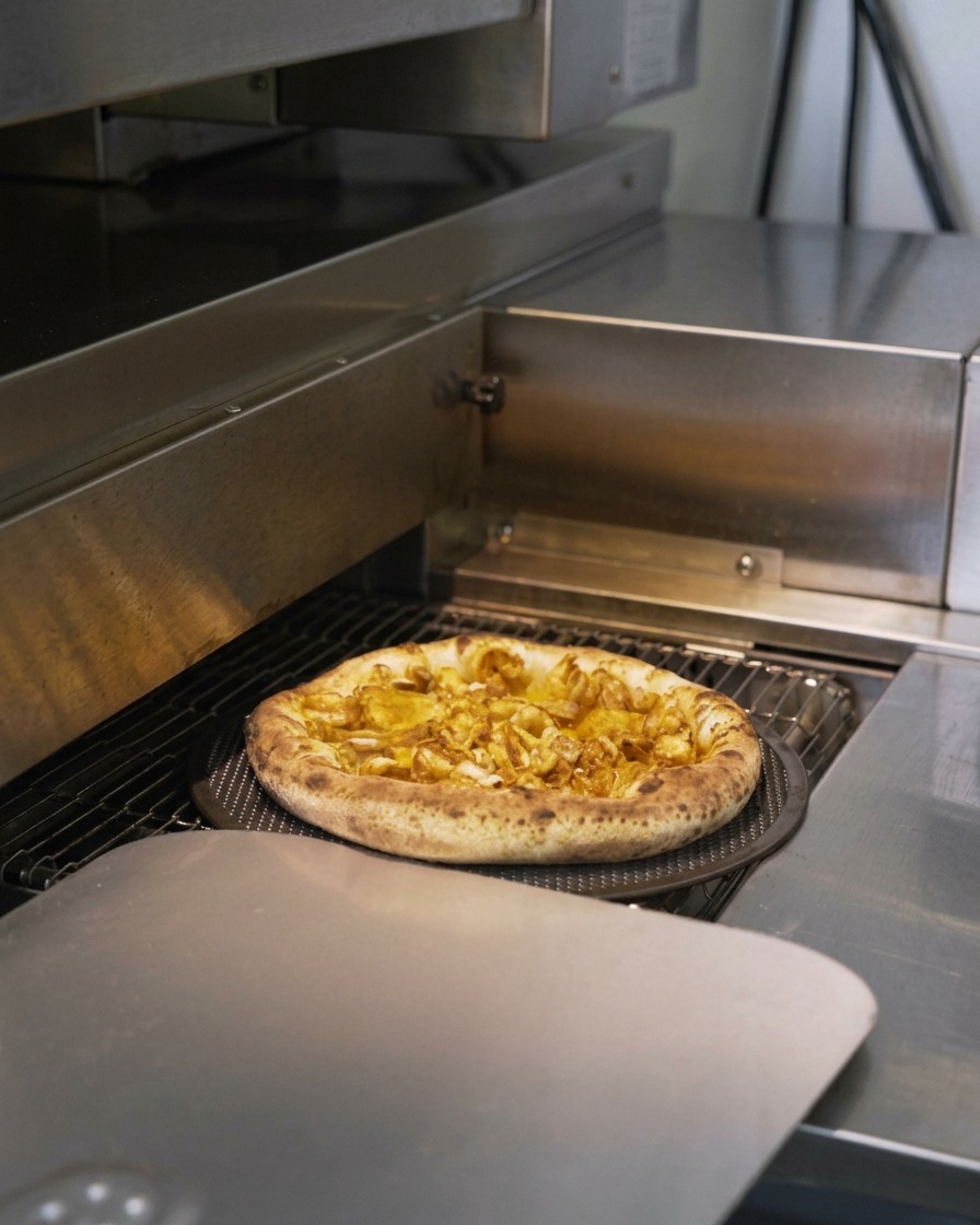 Una pizza de mariscos moviéndose por un horno comercial con los bordes de la masa inflándose y dorándose.