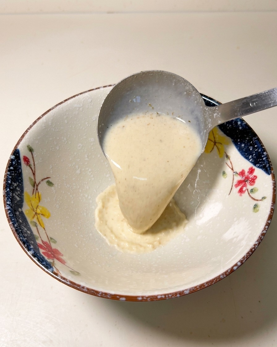 Un cucharón de metal vertiendo base de sopa de ramen caliente y cremosa en un cuenco de cerámica decorado.
