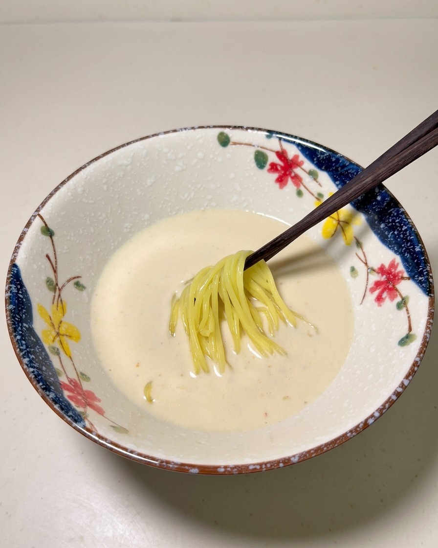 Fideos ramen amarillos ya cocidos colocándose en una base de sopa pálida y cremosa dentro de un cuenco decorativo.