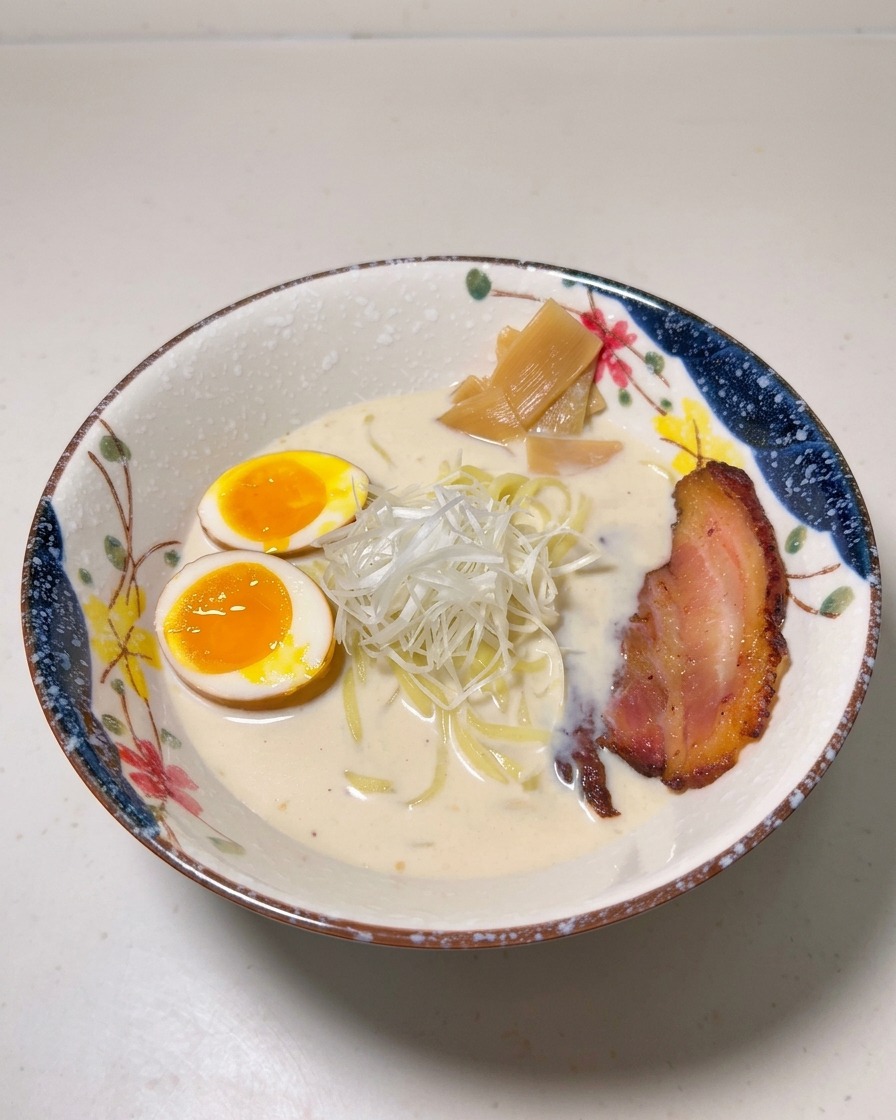 Un cuenco de ramen con huevos, brotes de bambú, cebolleta blanca en tiras y una rodaja de cerdo chashu dorado.