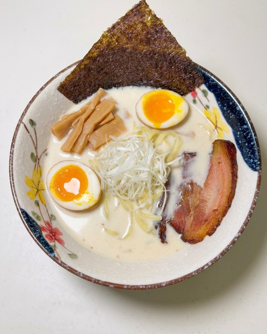Una hoja de alga nori oscura colocada en el borde de un cuenco de ramen completo.