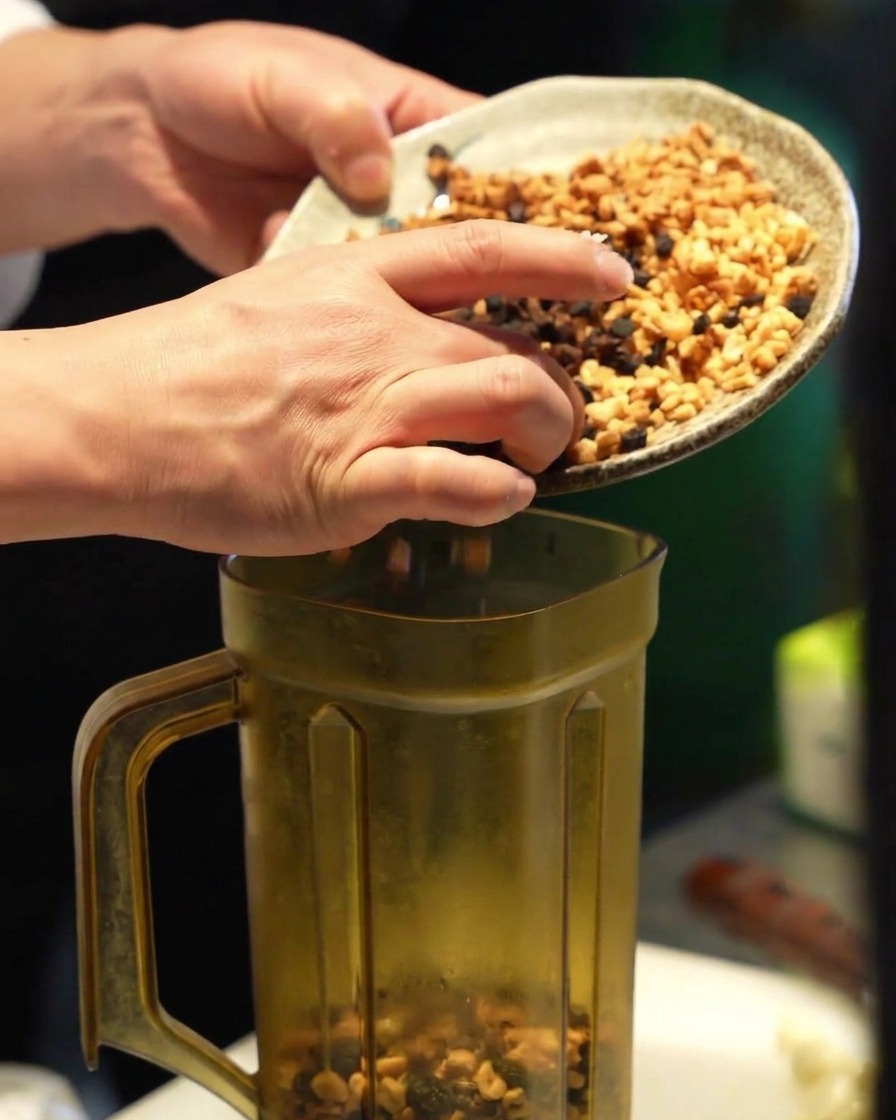 Manos pasando una mezcla de ajo frito de distintos colores al vaso de una licuadora transparente.