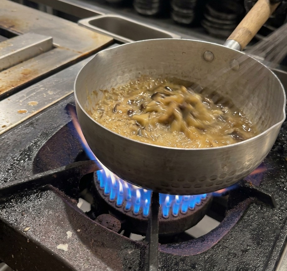 Un batidor de varillas removiendo continuamente una salsa espesa y marrón oscuro en una olla.