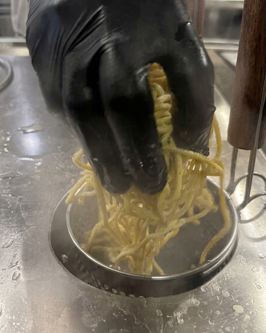Una mano introduciendo fideos amarillos en una olla con agua hirviendo.