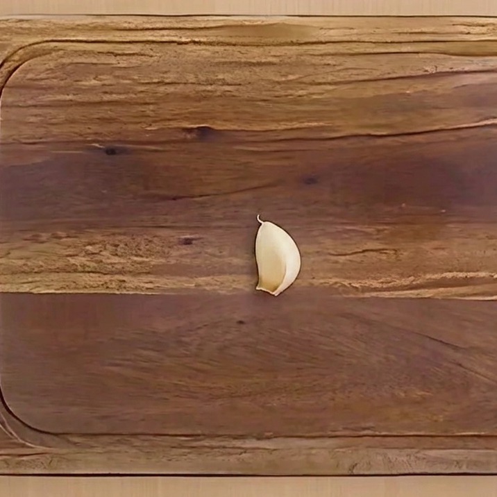 Un diente de ajo pelado, cortado por la mitad y sin el germen interno, sobre una tabla de madera.