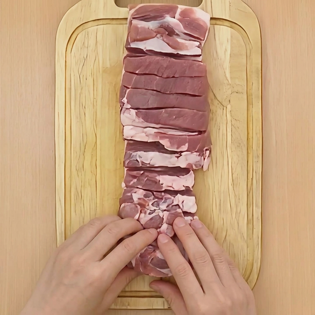 Dos manos enrollando firmemente un bloque de panceta de cerdo en forma cilíndrica sobre una tabla de madera.