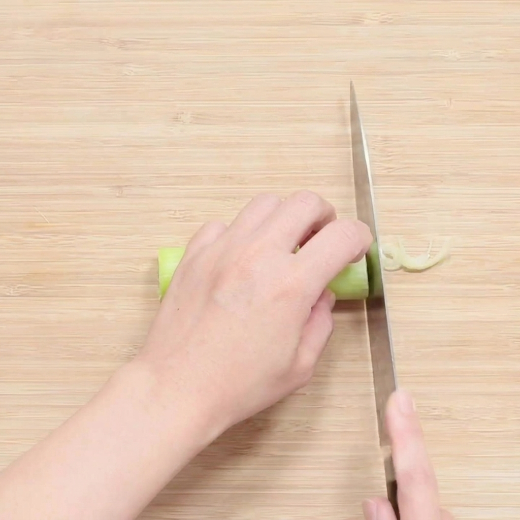 Manos cortando finamente la parte blanca de una cebolleta sobre una tabla de madera.