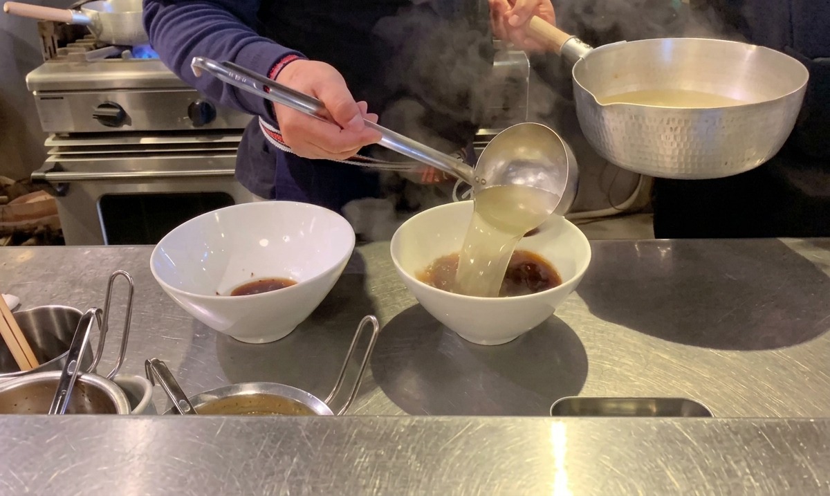 Vertiendo caldo caliente y transparente humeante en cuencos de ramen sobre la salsa de soja oscura.