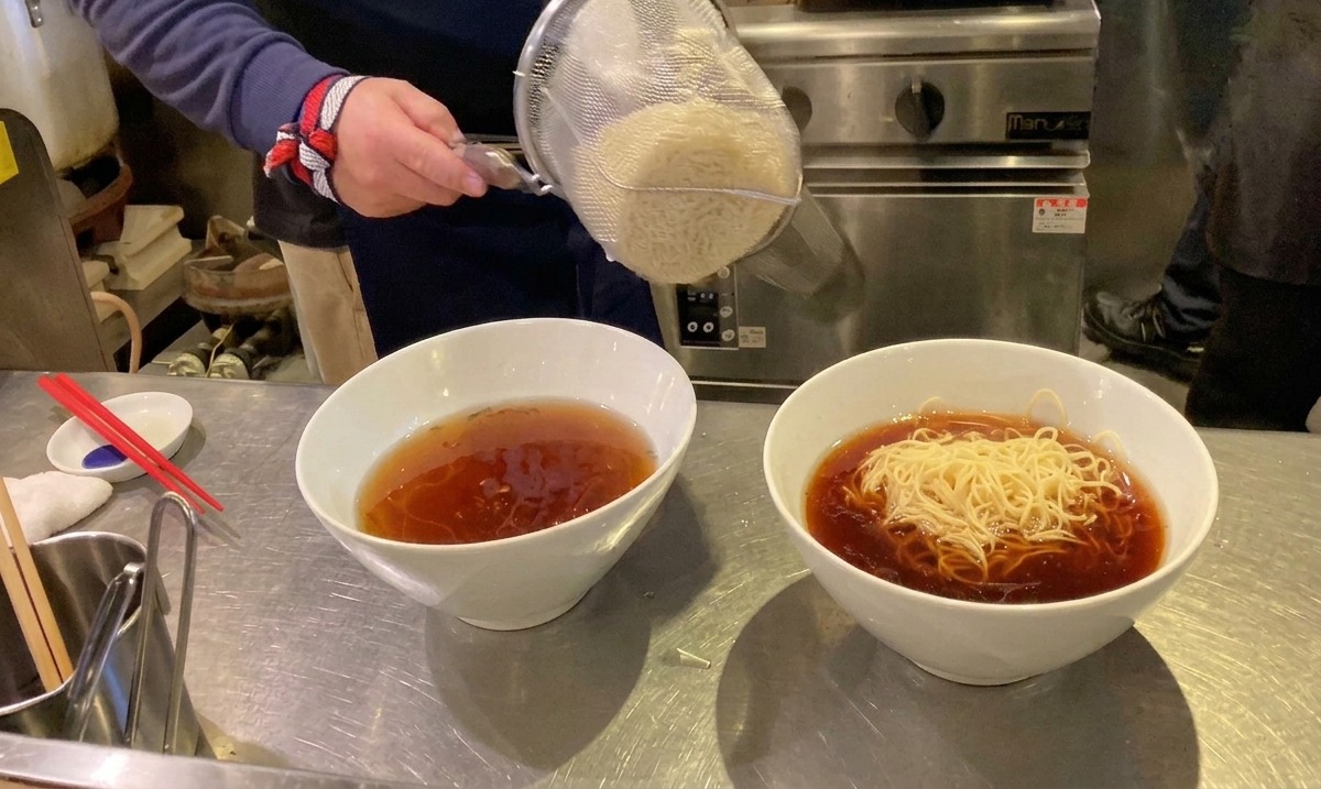 Fideos ramen recién cocidos cayendo desde un colador en un cuenco de sopa caliente.
