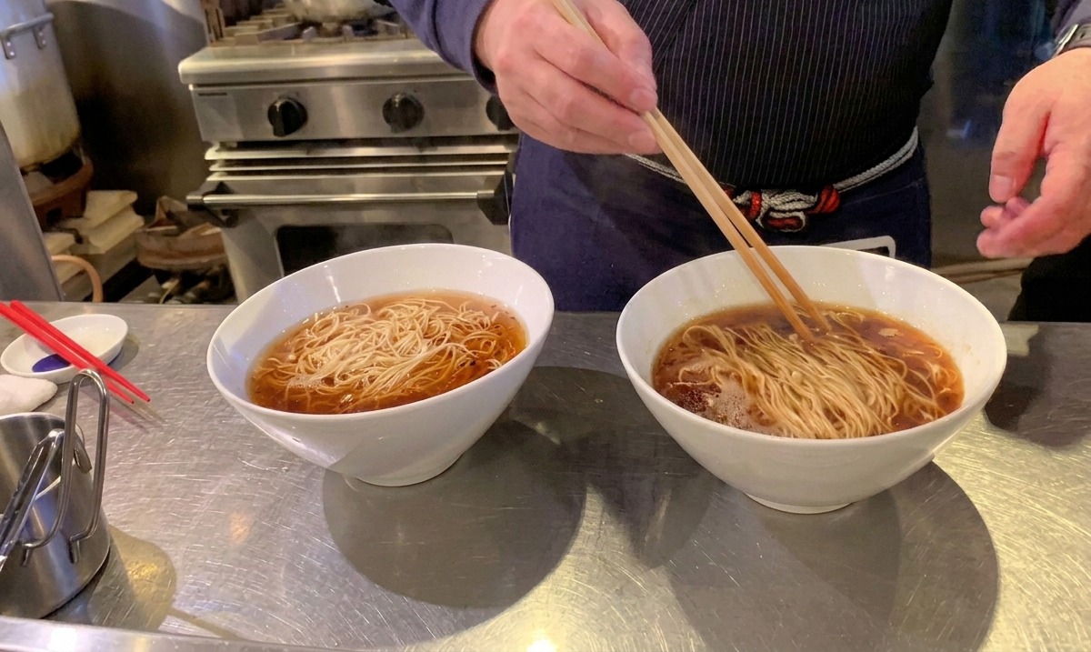 Usando palillos largos de madera para doblar y organizar los fideos ramen perfectamente dentro del caldo.