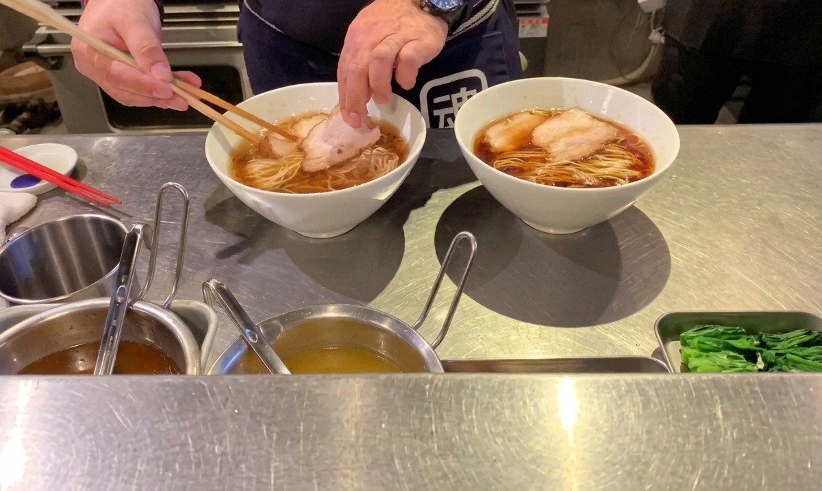 Cocinero colocando rodajas de chashu de cerdo cocinado sobre los fideos ramen con palillos.