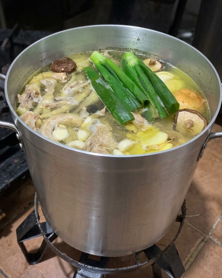 Olla con caldo de huesos hirviendo junto a cebolletas, rodajas de jengibre, setas shiitake y mitades de manzana.