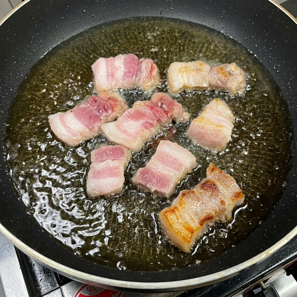 Cortes gruesos de panceta de cerdo friéndose en aceite, mostrando superficies doradas y caramelizadas.