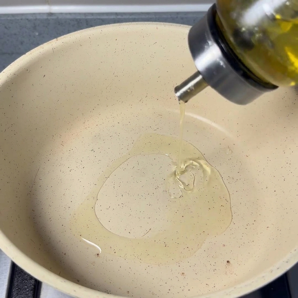 Vertiendo aceite de cocina neutro desde una botella de vidrio a una sartén clara.