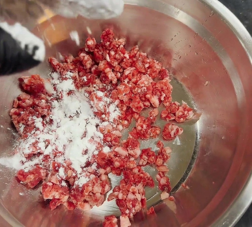 Almidón de maíz blanco espolvoreado sobre una pila de carne picada fresca en un bol de acero inoxidable.