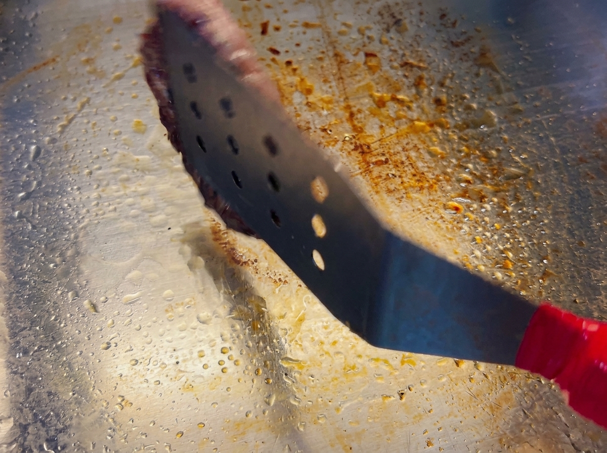 Una espátula de metal levantando una hamburguesa para darle la vuelta, mostrando una costra dorada y caramelizada.