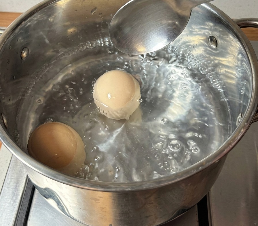 Dos huevos marrones enteros hirviendo vigorosamente en una olla de acero inoxidable con agua burbujeante.