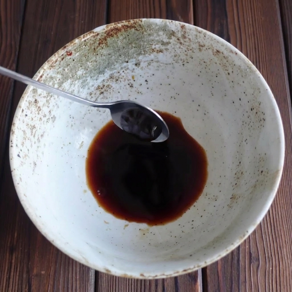 Cuchara añadiendo salsa de ostras espesa a un cuenco con salsa de soja.